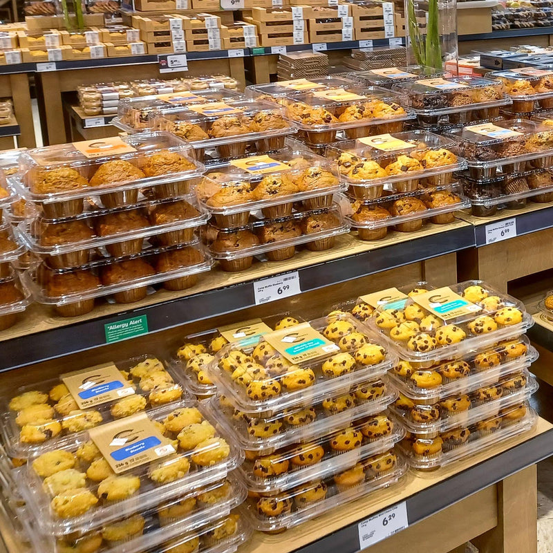 Packages of bakery muffins on a grocery store wooden display table